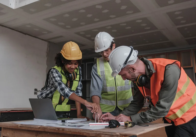 Civil engineering team wearing safety helmets, meeting and collaborating while reviewing plans at a construction site.