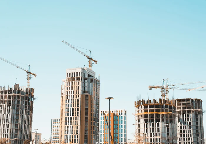 Tower cranes operating above a large construction site with a multi-story building structure in progress.