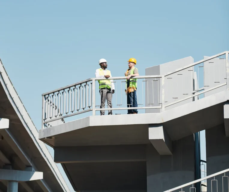 Engineers in safety helmets reviewing blueprints and discussing details of a construction project on site.