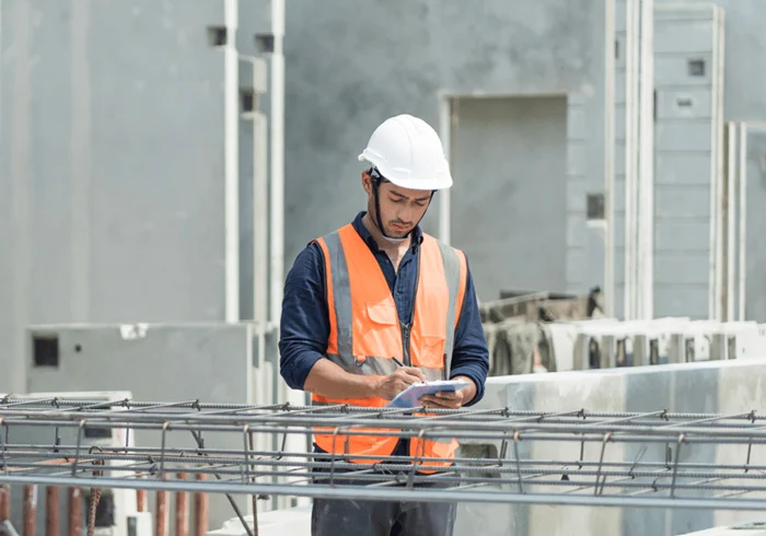 Male engineers wearing safety helmets inspecting equipment and reviewing plans at an industrial or construction site.